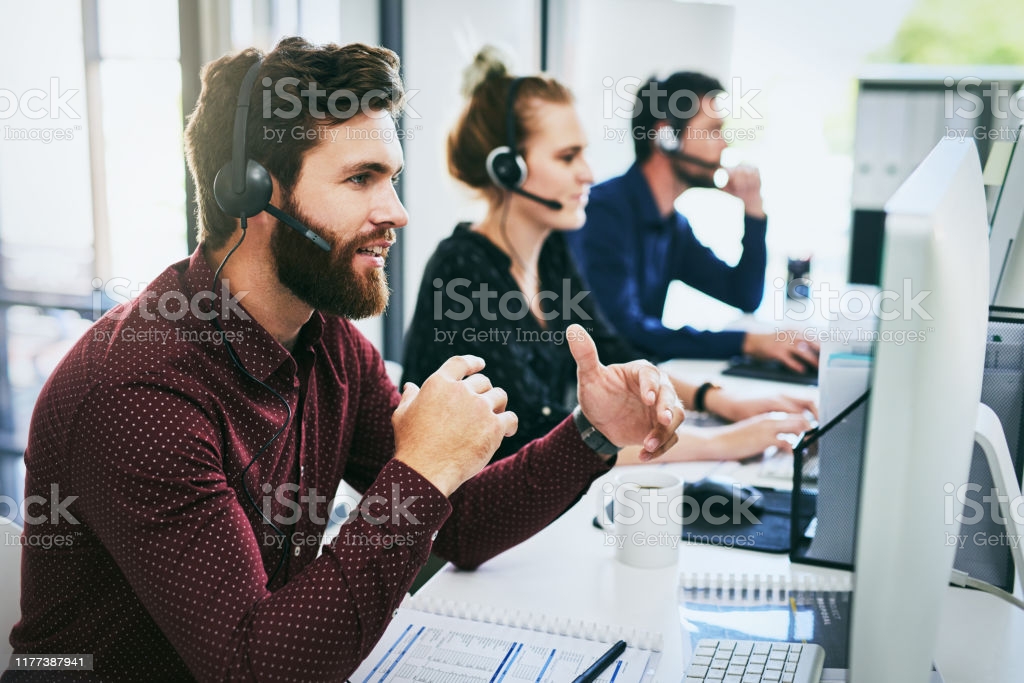 Cropped shot of a handsome young businessman wearing a headset and using a computer while sitting with his colleagues